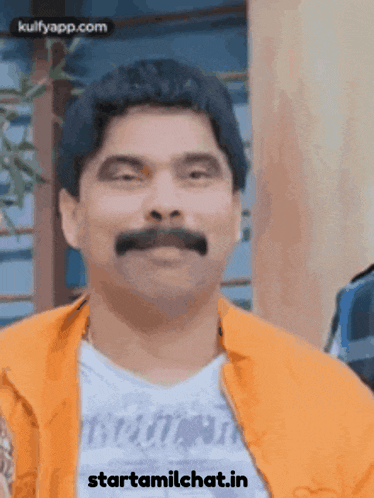 a man with a mustache is wearing an orange jacket and a white shirt with the words starttamilchat.in on the bottom