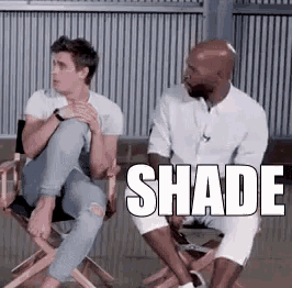 two men are sitting in director 's chairs talking to each other and the word shade is on the screen .