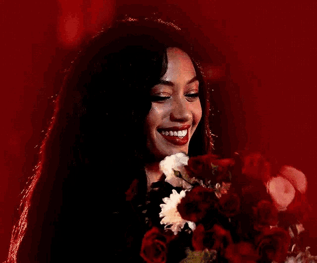 a woman is smiling while holding a bouquet of red flowers .