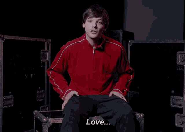 a young man in a red jacket is sitting on a trunk and says love