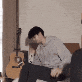 a man is sitting on a couch with his legs crossed in front of a guitar