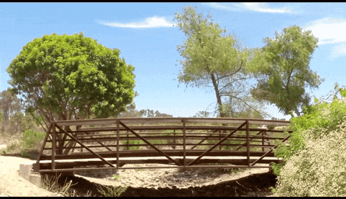 a wooden bridge with trees in the background and a blue sky