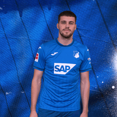 a man in a blue shirt with the word sap on it gives two thumbs up