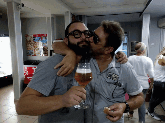 a man holding a glass of beer is kissed by another man