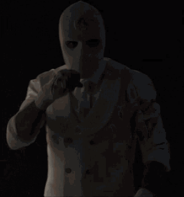 a man wearing a white mask and gloves is standing in the dark
