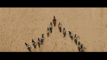 a group of men riding horses in a field with mountains behind them