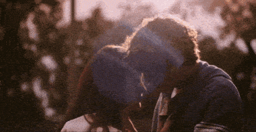 a man and a woman are kissing with the sun shining through the trees in the background