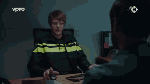 a police officer sits at a desk talking to a man on a tv show