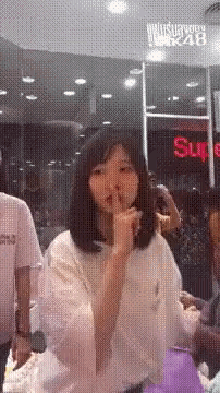 a woman is holding her finger to her mouth in front of a sign that says sure .