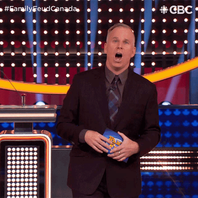 a man in a suit and tie stands in front of a podium with his mouth open and a cbs logo behind him