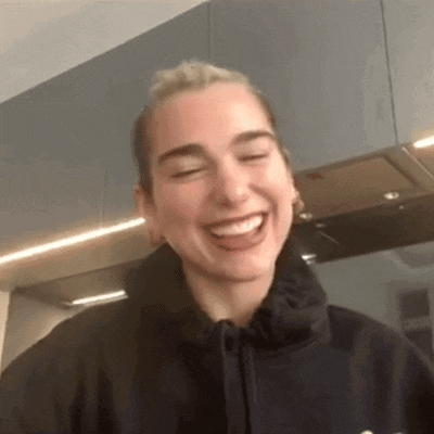 a woman in a black hoodie is laughing with her eyes closed in a kitchen .