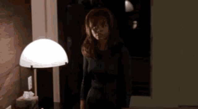 a woman is standing in a dark room with a lamp and a box of tissues .