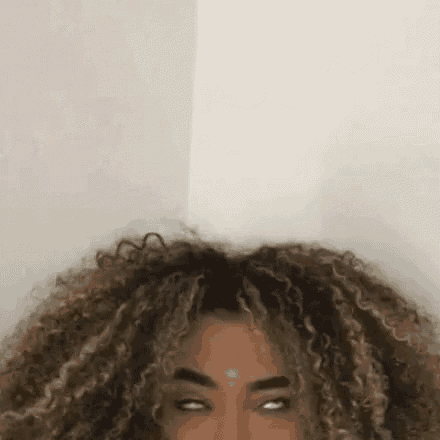 a woman with curly hair is making a funny face while looking at the camera .
