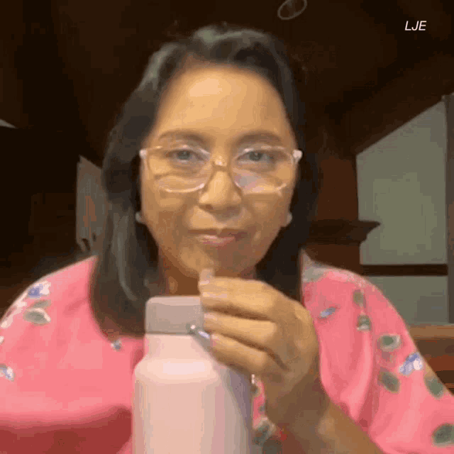 a woman wearing glasses and a pink shirt is drinking from a bottle