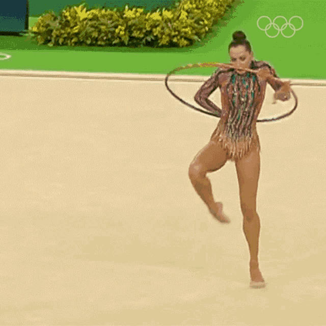 a rhythmic gymnast performs with a hula hoop in front of the olympic symbol