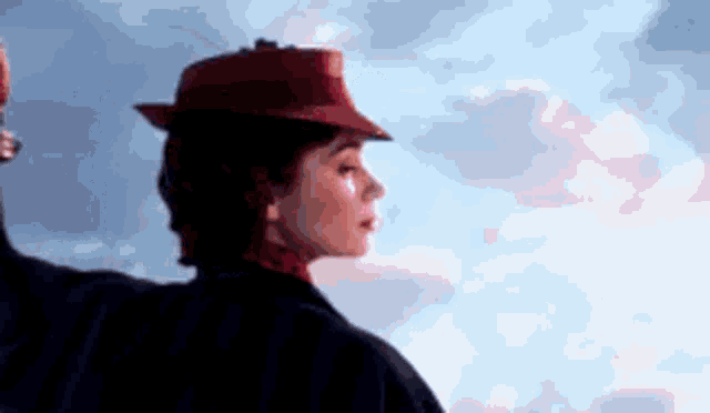 a woman wearing a red hat is standing in front of a cloudy sky .