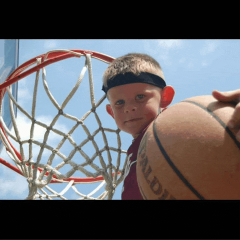 a young boy holding a spalding basketball in front of a basketball net
