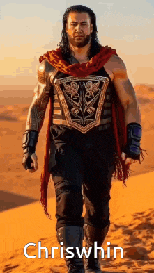 roman reigns is walking in the desert wearing a red scarf and a shield .