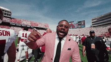 a man in a suit and tie is pointing at a football player with the number 11 on his shirt