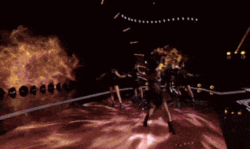 a group of women are dancing on a stage with a fire background