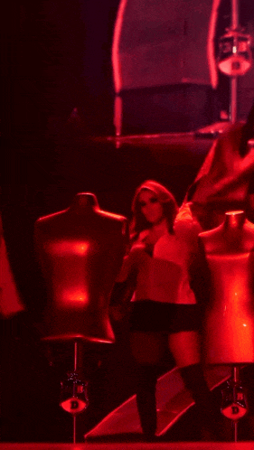 a woman is standing on a stage in front of mannequins in red light