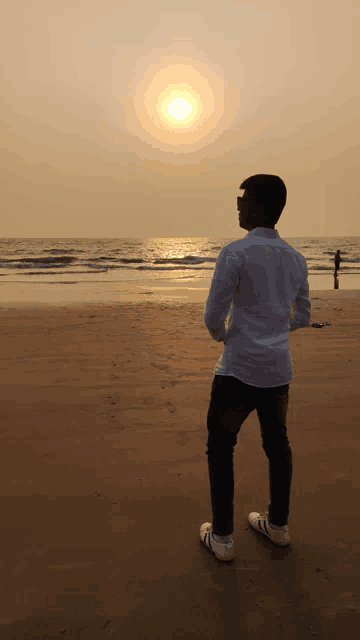 a man standing on a beach looking at the sun setting