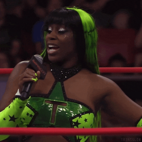 a woman in a green top with the number 7 on it is holding a microphone in a ring