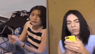 two women are sitting next to each other one is holding a bottle of water and the other is holding a cell phone