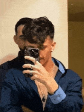 a man taking a picture of himself in a mirror with another man behind him