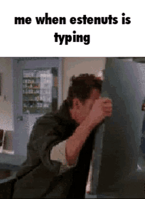 a man covering his face with his hands while typing on a computer .