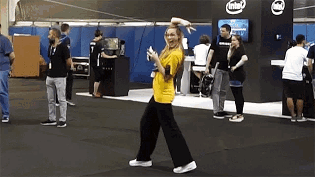 a woman in a yellow shirt dancing in front of an intel booth