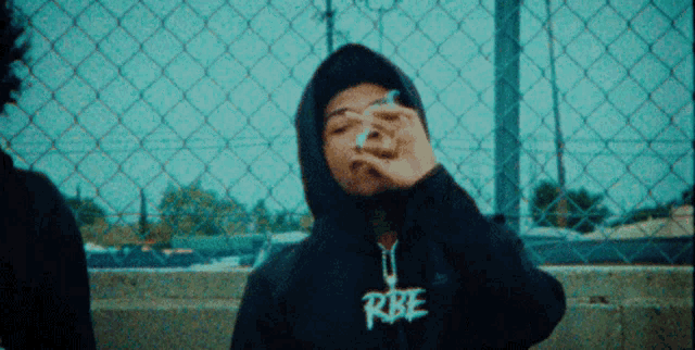 a person wearing a hoodie that says rbe smoking a cigarette