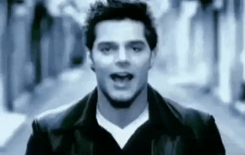 a man in a black jacket and white t-shirt is singing in a video .
