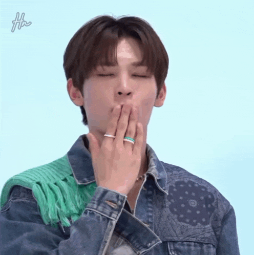 a man wearing a denim jacket and a green scarf is covering his mouth with his hands