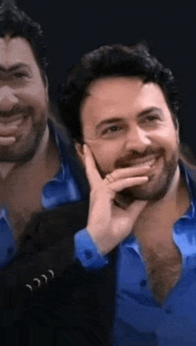 a man with a beard is wearing a blue shirt and a black jacket .