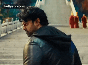 a man in a black leather jacket is walking down a set of stairs in front of a group of monks .