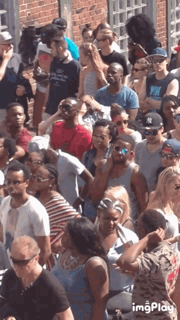a crowd of people including a man wearing a ny hat and sunglasses