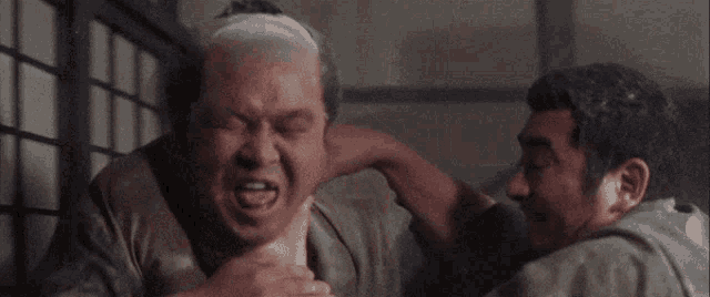 two men are fighting in a room and one of them is holding the other 's neck .