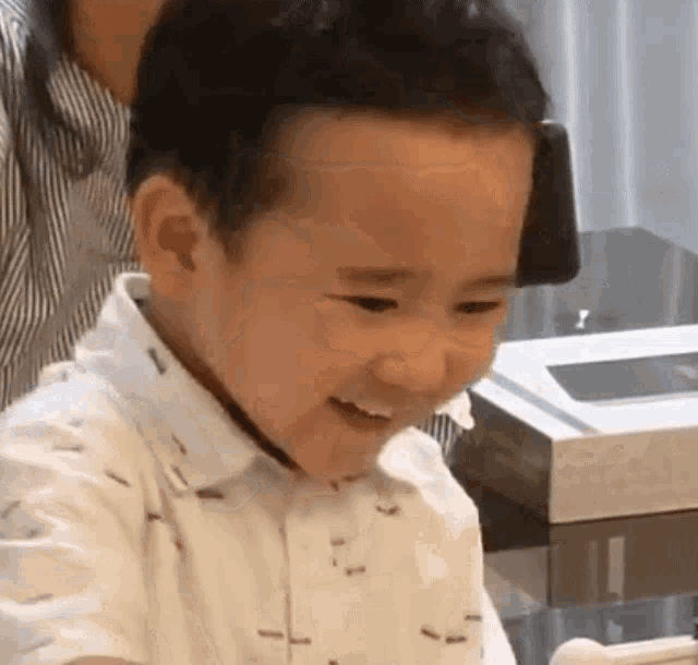 a little boy in a white shirt is smiling while sitting at a table with a woman .