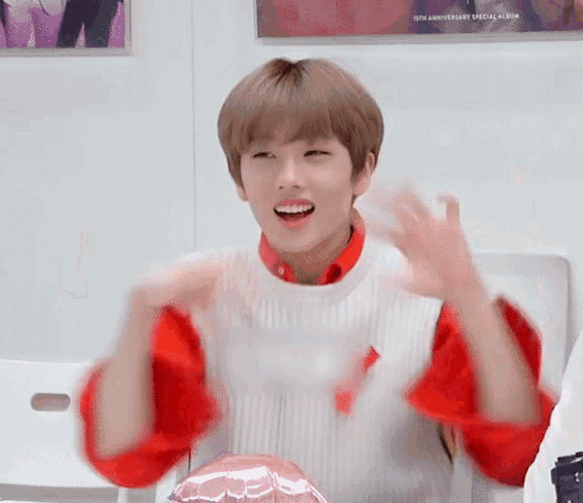 a young man wearing a red shirt and a white vest is sitting on a chair and making a funny face .