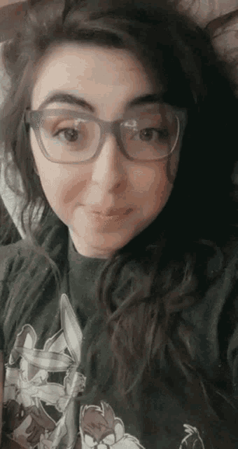 a woman wearing glasses and a looney tunes shirt is taking a selfie