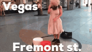 a woman in a white dress is standing next to a red bucket on fremont st.