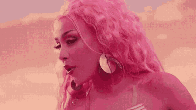 a woman with pink hair and earrings is standing in front of a pink background .
