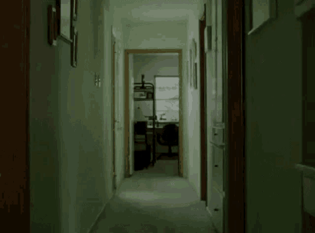 a long hallway with green walls leading to a bedroom with a bunk bed and a desk .