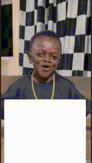 a young boy with a gold chain around his neck is sitting on a couch in front of checkered curtains