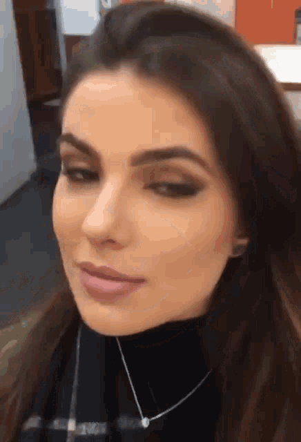 a woman wearing a black turtleneck and a necklace looks at the camera