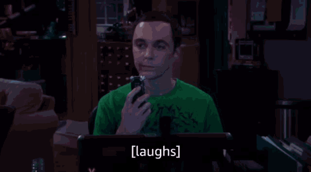 a man in a green shirt is laughing while holding a cellphone
