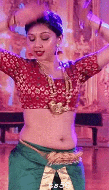 a woman in a red blouse and green skirt is dancing on a stage .