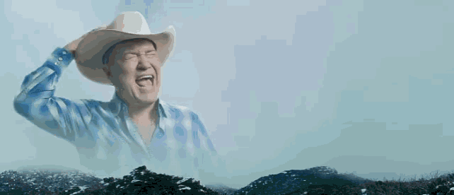 a man in a cowboy hat and suit is standing in front of a hill .