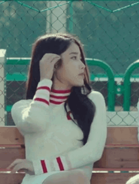 a woman in a white sweater with red and white stripes on the sleeves is sitting on a bench